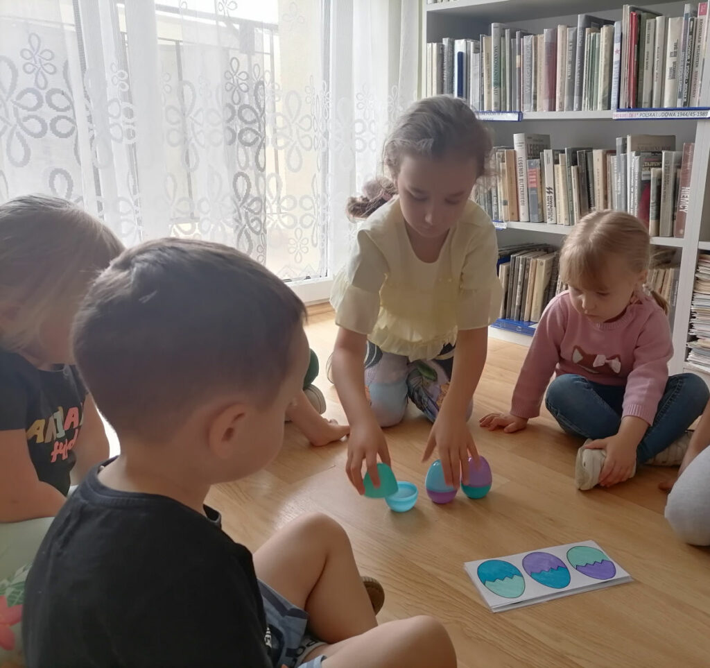 Na zdjęciu widoczna jest grupa 4 przedszkolaków podczas zabawy schematycznej z kolorowymi, plastikowymi jajkami.