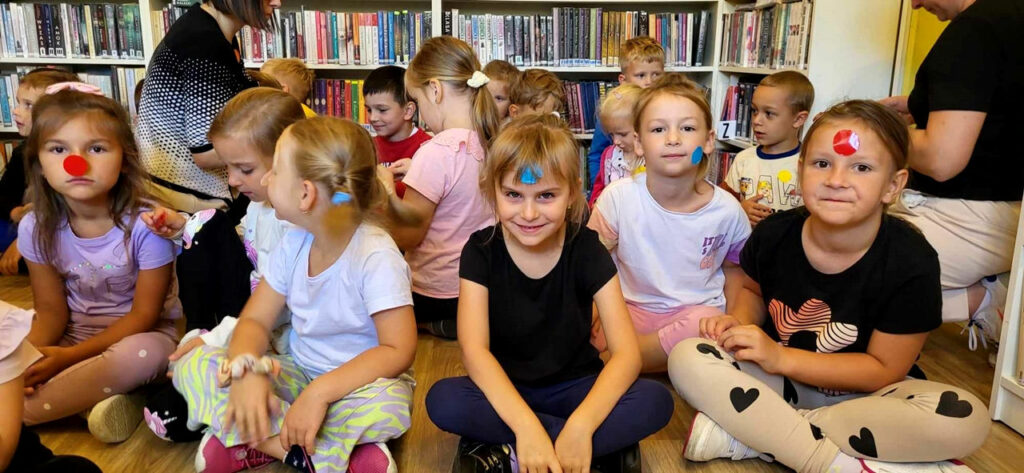Na zdjęciu widać dzieci siedzące na podłodze. Dzieci mają naklejone papierowe kropki.