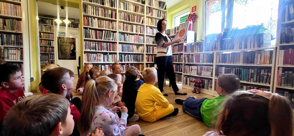na zdjęciu widać bibliotekarkę pokazującą dzieciom książkę