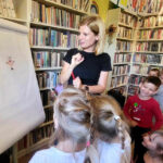 na zdjęciu widać bibliotekarkę pokazującą dzieciom ilustracje