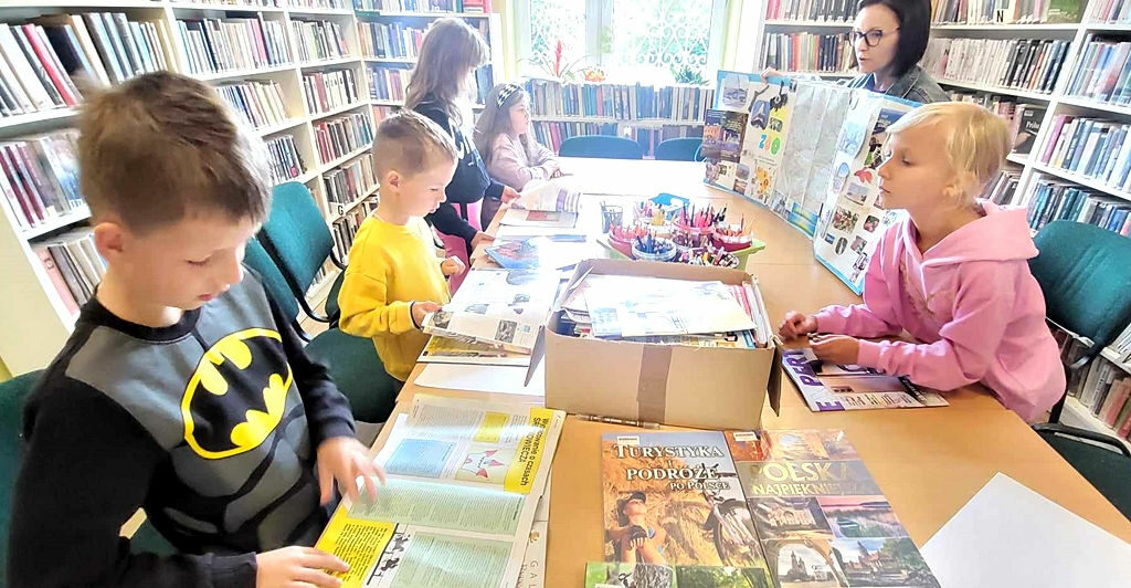 na zdjęciu widać bibliotekarkę pokazująca dzieciom ilustracje wycięte z gazet