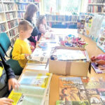 na zdjęciu widać bibliotekarkę pokazująca dzieciom ilustracje wycięte z gazet