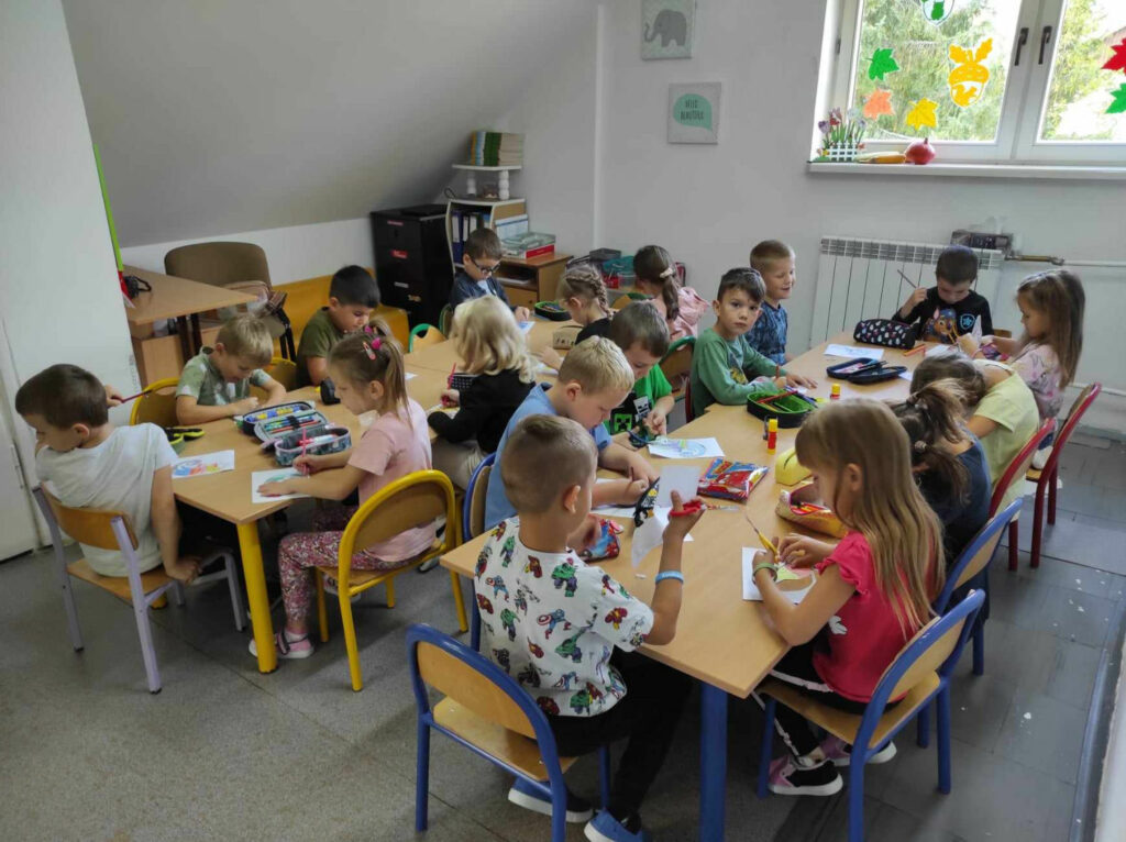na zdjęciu widać salę przedszkolną, dzieci siedzą przy stolikach, wykonują pracę plastyczną