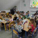 na zdjęciu widać salę przedszkolną, dzieci siedzą przy stolikach, wykonują pracę plastyczną
