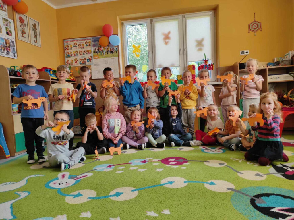 na zdjęciu widać salę przedszkolną, dzieci prezentują wykonane prace plastyczne.