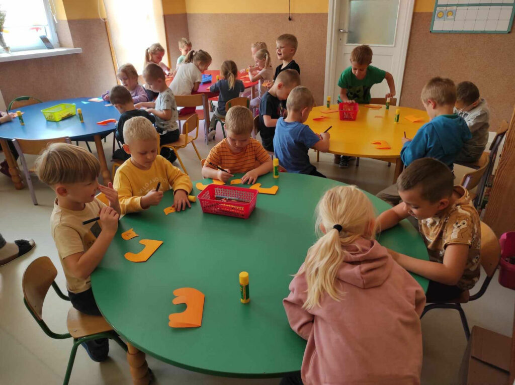 na zdjęciu widać salę przedszkolną, dzieci siedzą przy stolikach, wykonują pracę plastyczną