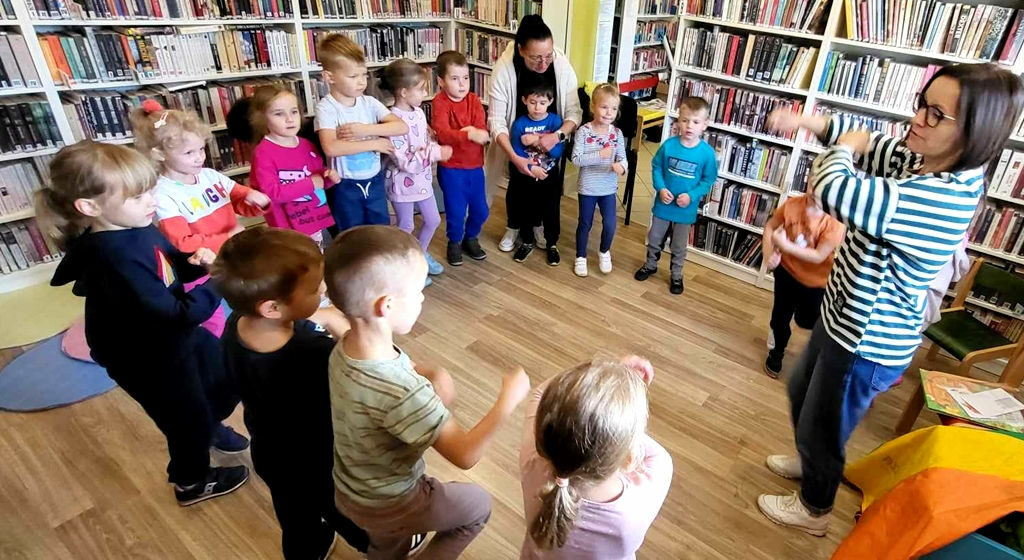 na zdjęciu widać dzieci w sali bibliotecznej stojące w kole