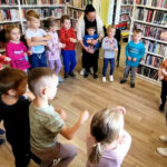 na zdjęciu widać dzieci w sali bibliotecznej stojące w kole