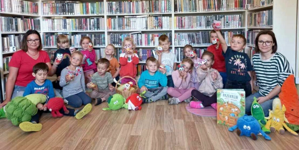 na zdjęciu widać dzieci i bibliotekarki siedzące na ziemi.