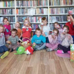 na zdjęciu widać dzieci i bibliotekarki siedzące na ziemi.
