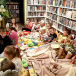 na zdjęciu widać dzieci siedzące na podłodze w sali bibliotecznej.