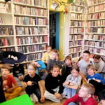 na zdjęciu widać dzieci siedzące na podłodze oraz stojąca przed nimi bibliotekarkę