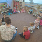 dzieci z przedszkola Montessori siedzą na dywanie i słuchają bajki czytanej przez bibliotekarza
