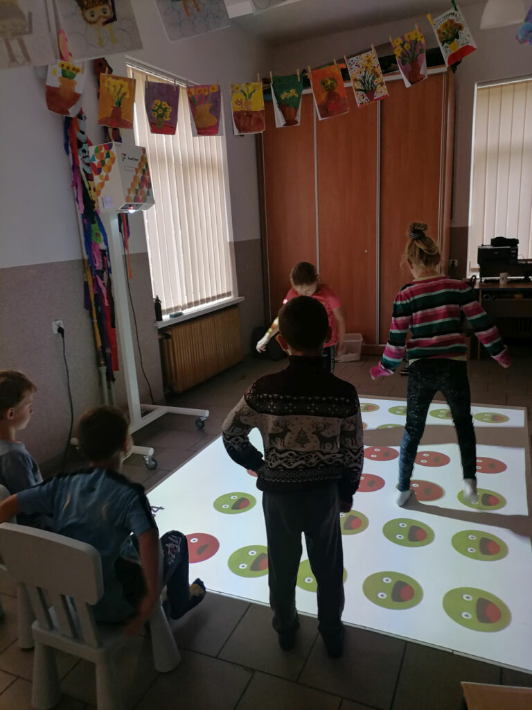 na zdjęciu widoczna jest grupa 5 dzieci (2 dziewczynki i 3 chłopców) podczas zabawy na multimedialnej podłodze FunFloor.