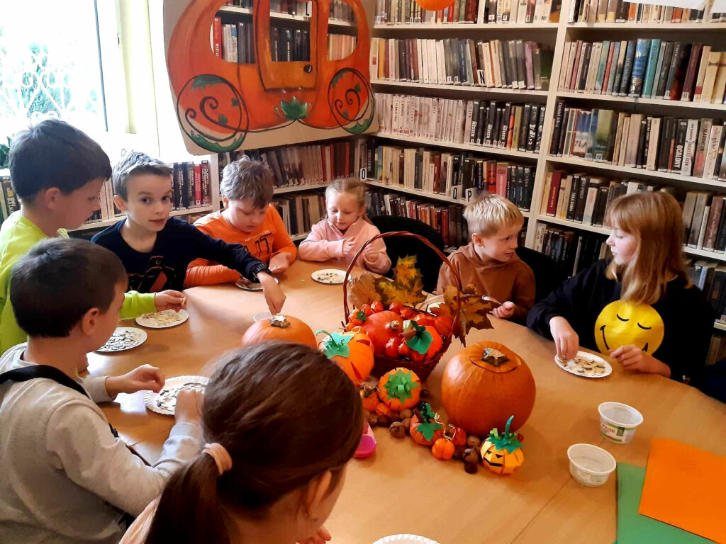 na zdjęciu widać dzieci siedzące wokół stołu w sali bibliotecznej
