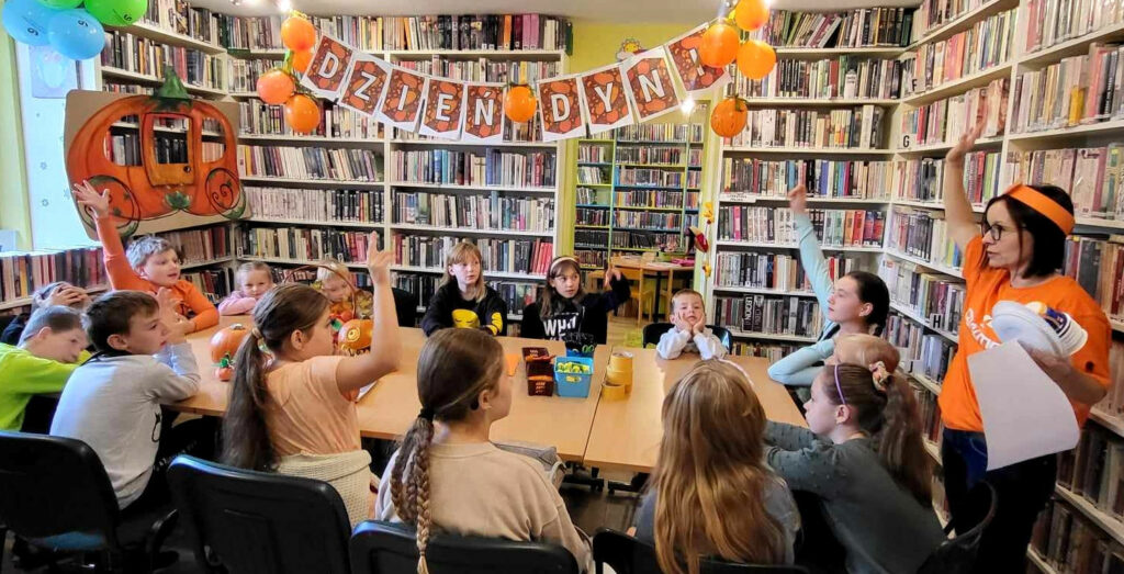na zdjęciu widać dzieci siedzące wokół stołu w sali bibliotecznej