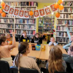 na zdjęciu widać dzieci siedzące wokół stołu w sali bibliotecznej