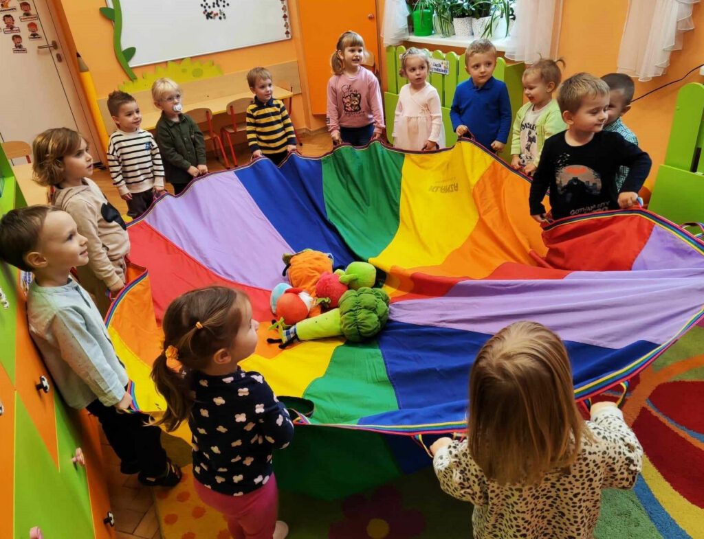 na zdjęciu widać dzieci trzymające kolorową chustę zabawową