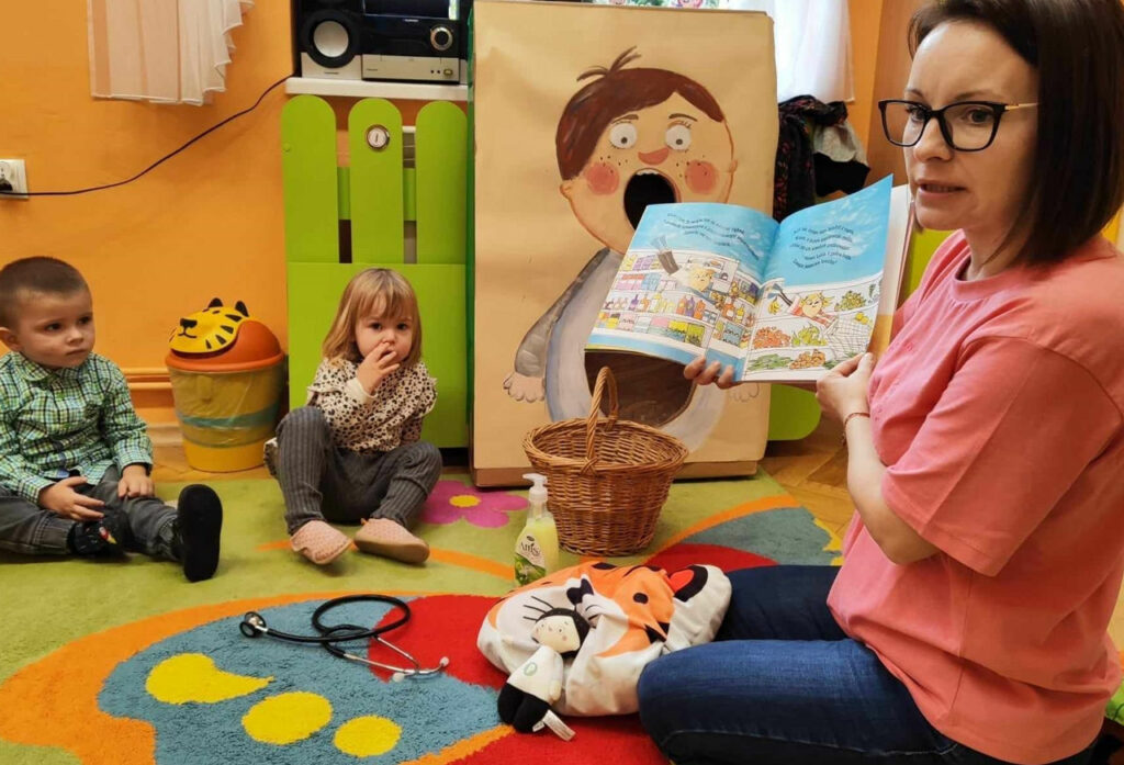 na zdjęciu widać bibliotekarkę czytającą dzieciom książkę