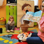 na zdjęciu widać bibliotekarkę czytającą dzieciom książkę