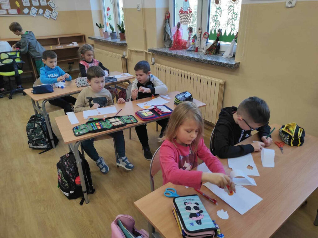 na zdjęciu widać salę szkolną, dzieci siedzą przy stolikach, wykonują pracę plstyczną
