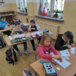 na zdjęciu widać salę szkolną, dzieci siedzą przy stolikach, wykonują pracę plstyczną