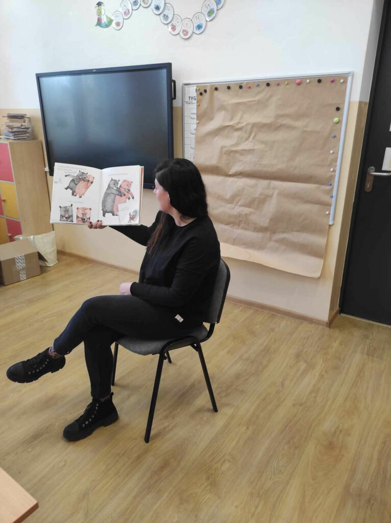 na zdjęciu widać bibliotekarza, czyta dzieciom książkę