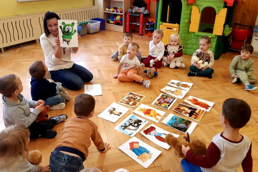 na zdjęciu widać dzieci siedzące na podłodze a przed nimi ilustracje przedstawiające misie z bajki.