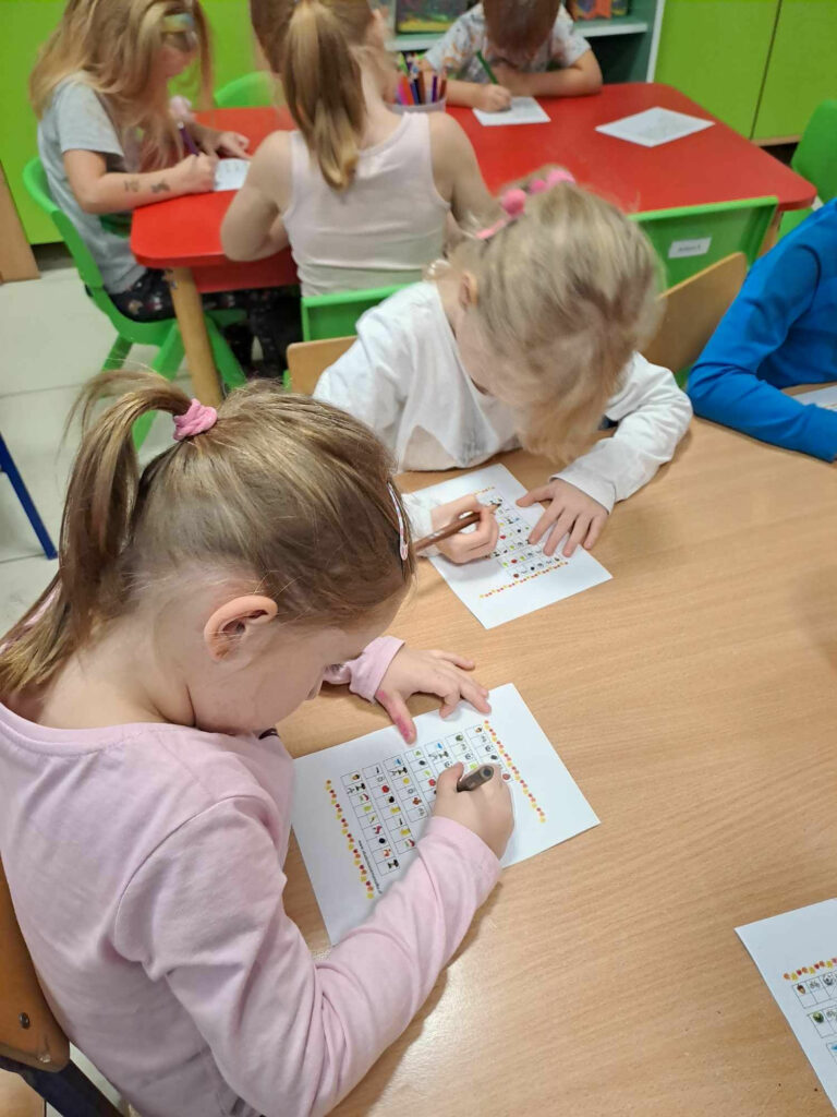 Przy stolikach siedzą dzieci i wykonuja prace plastyczne.