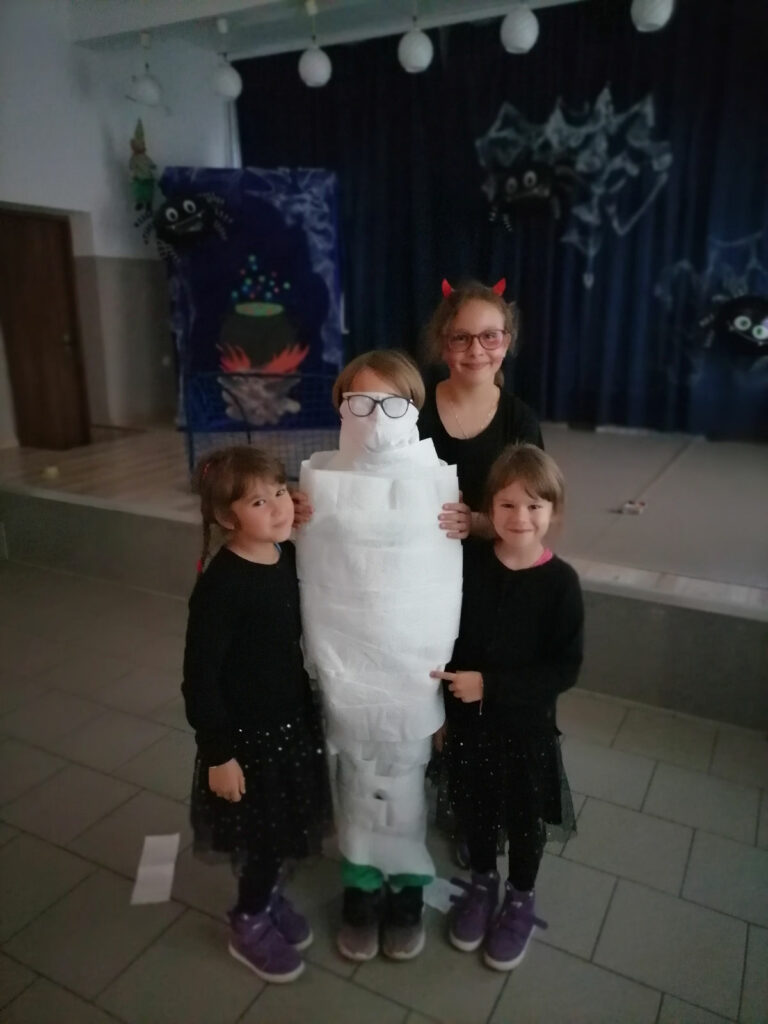 Na zdjęciu widoczne są 4 dziewczynki jedna z nich owinięta papierem toaletowym na podobieństwo mumii.