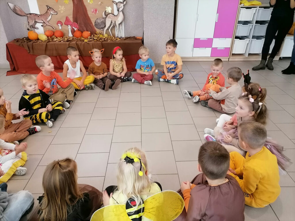 Na zdjęciu widoczna jest grupa 18 dzieci w kolorowych strojach biorących udział w zabawie gorąca dynia.