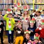 Zdjęcie przedstawia dzieci w czapkach elfów stojące na tle regału z książkami