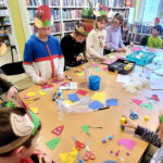 na zdjęciu widać dzieci siedzące wokół stołu w sali bibliotecznej