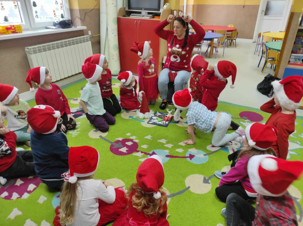 na zdjęciu widać salę przedszkolną, dzieci siedzą w kole na dywanie, słuchają opowiadania