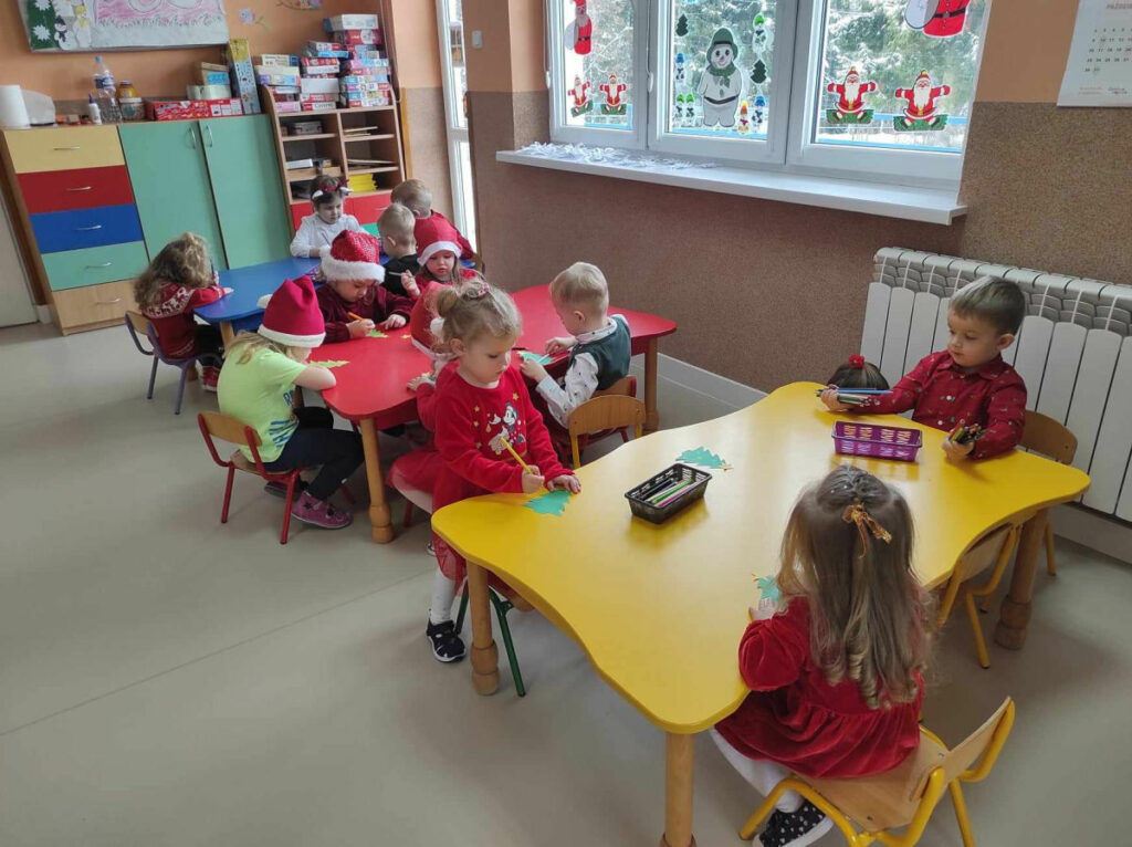 na zdjęciu widać salę przedszkolną, dzieci siedzą przy stolikach, wykonują pracę plastyczną