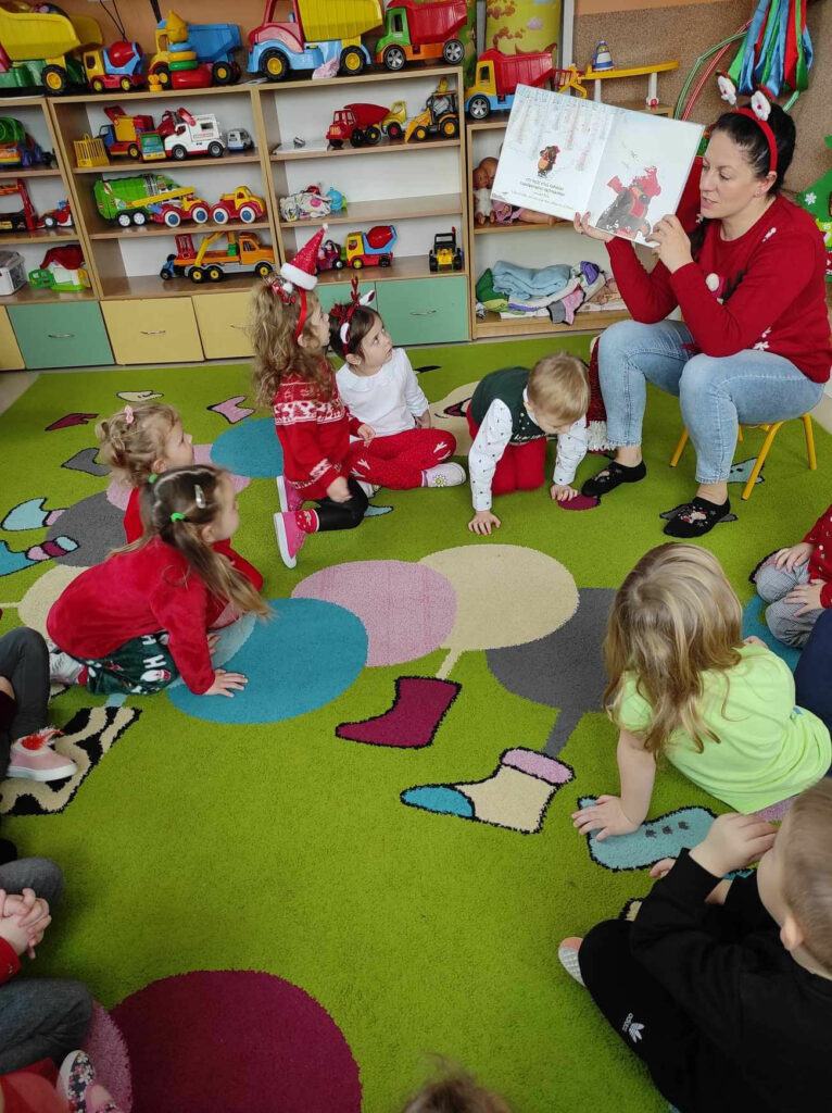 na zdjęciu widać salę przedszkolną, dzieci siedzą na dywanie, słuchają opowiadania