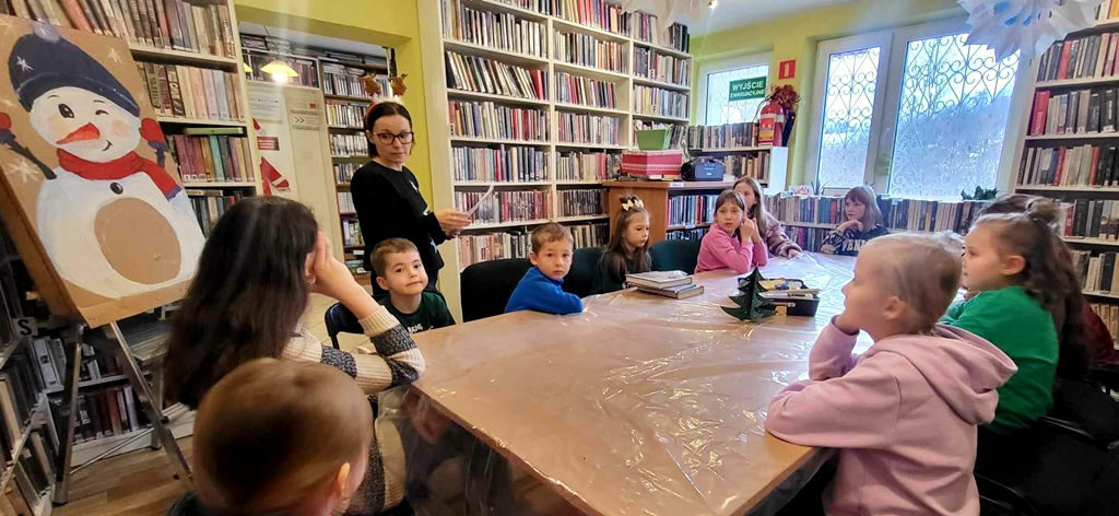 na zdjęciu widać dzieci siedzące wokół stołu w sali bibliotecznej