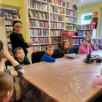 na zdjęciu widać dzieci siedzące wokół stołu w sali bibliotecznej