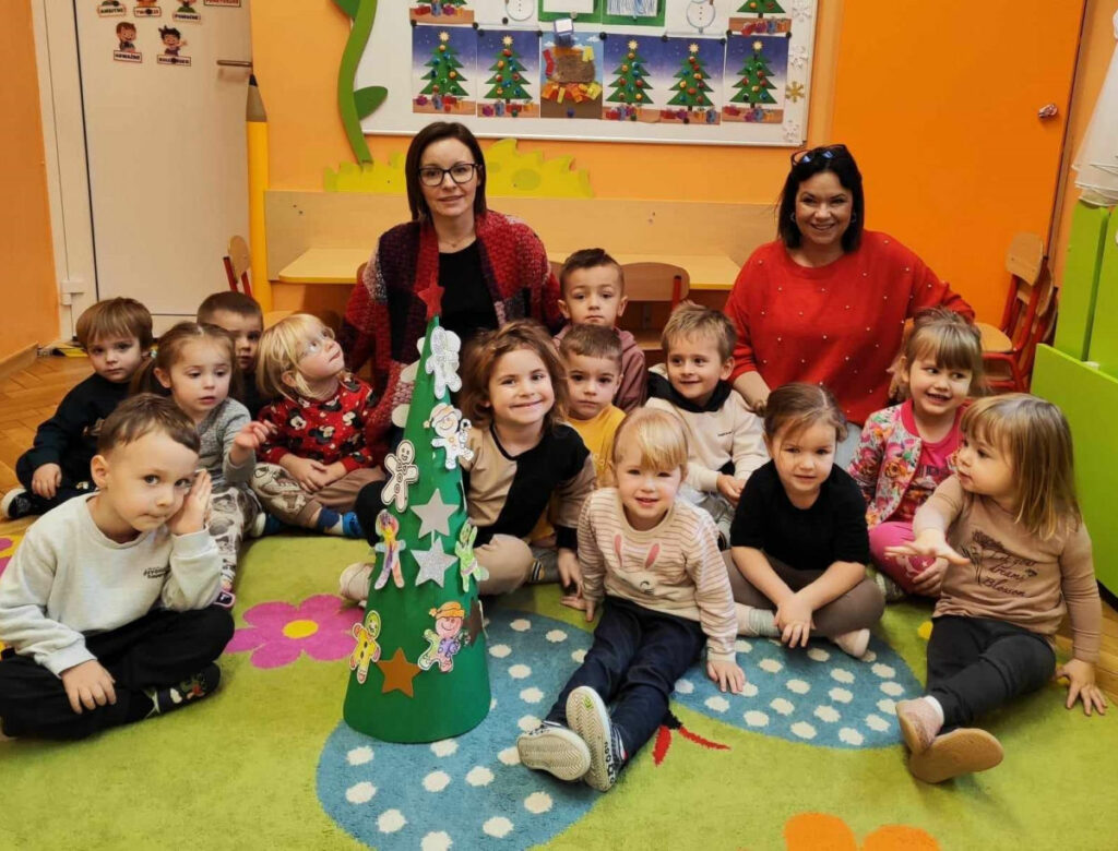 na zdjęciu widać dzieci oraz bibliotekarki siedzące na kolorowym dywanie