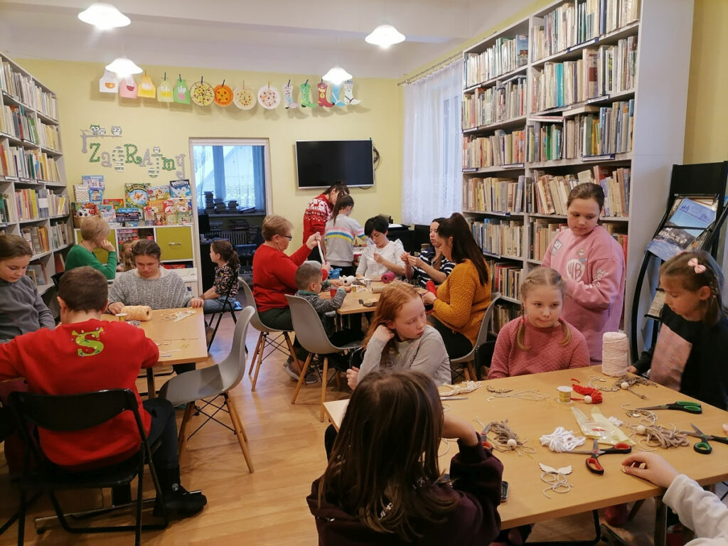 Na zdjęciu widocznych jest 6 osób dorosłych i 14 dzieci podczas wykonywania makramowych aniołków.