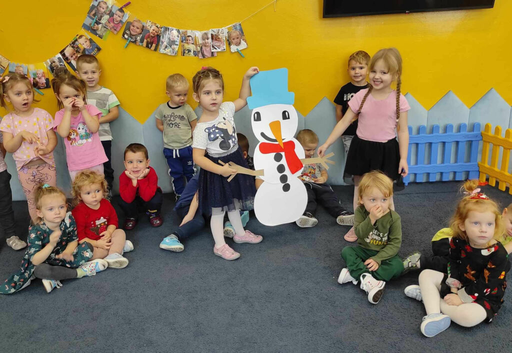 na zdjęciu widać salę przedszkolną, dzieci pozują do zdjęcia grupowego, prezentują wykonaną pracę