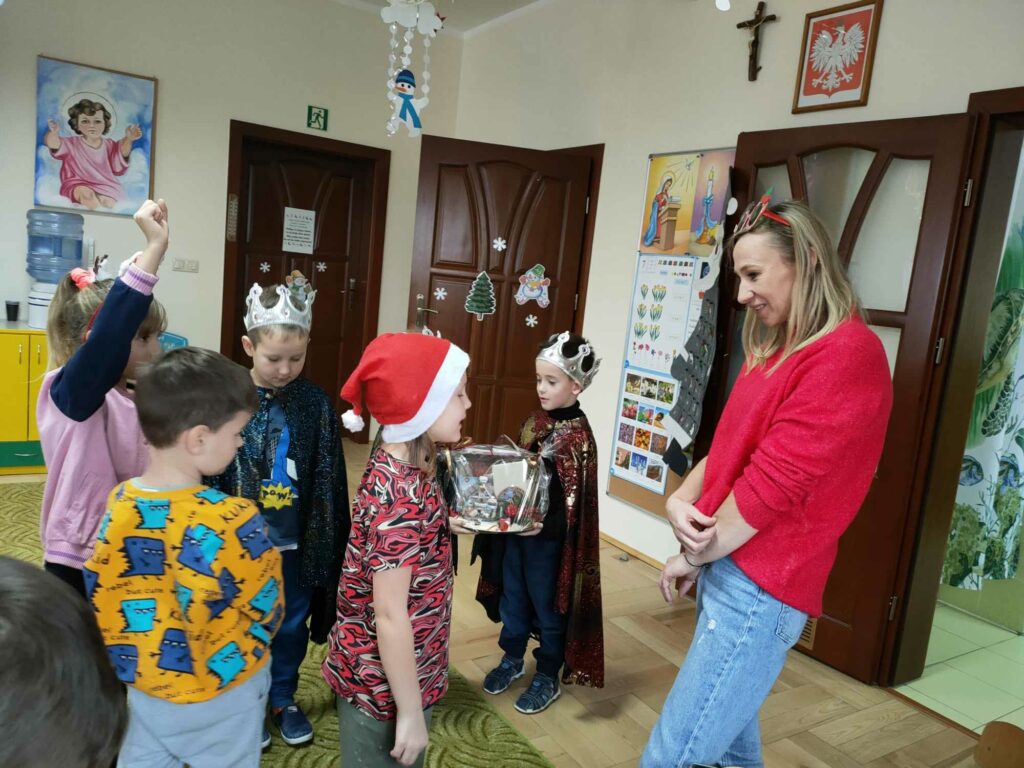 Na zdjęciu widocznych jest 5 przedszkolaków i bibliotekarz podczas składania życzeń świątecznych.
