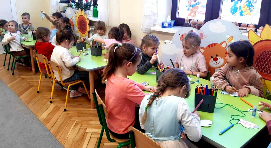 na zdjęciu widać dzieci siedzące przy zielonych stolikach