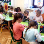 na zdjęciu widać dzieci siedzące przy zielonych stolikach
