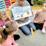 na zdjęciu widać bibliotekarkę pokazującą dzieciom książkę