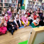 na zdjęciu widać dzieci w wieku przedszkolnym siedzące na podłodze w sali bibliotecznej