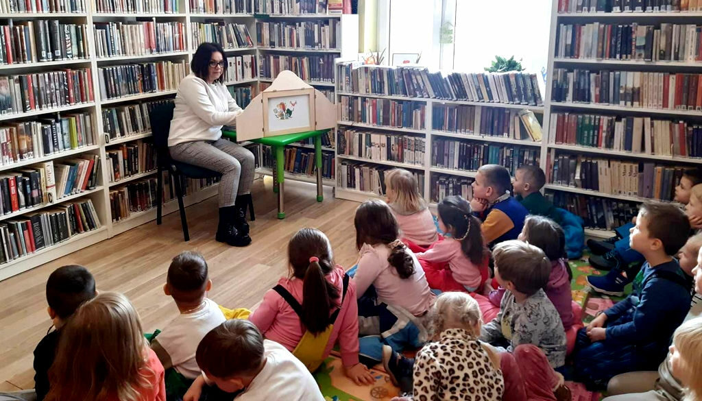na zdjęciu widać dzieci słuchające czytanej im bajki oraz bibliotekarkę siedząco na krześle