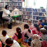 na zdjęciu widać dzieci słuchające czytanej im bajki oraz bibliotekarkę siedząco na krześle