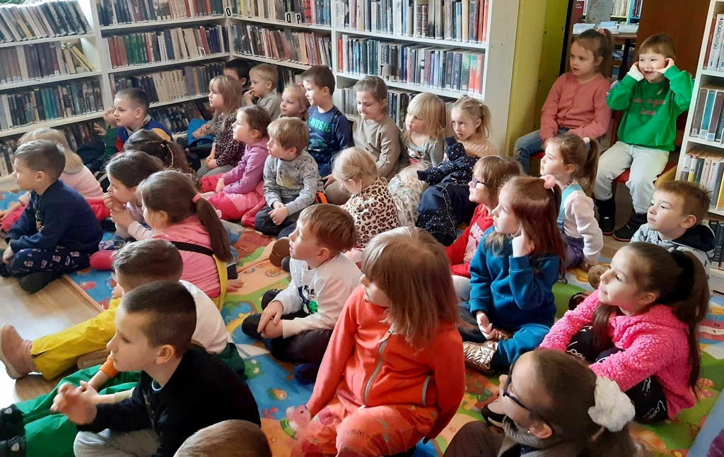 na zdjęciu widać dzieci w wieku przedszkolnym siedzące na podłodze w sali bibliotecznej