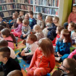na zdjęciu widać dzieci w wieku przedszkolnym siedzące na podłodze w sali bibliotecznej